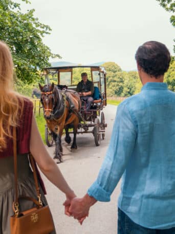 Una coppia che si tiene per mano mentre cammina nel Parco Nazionale di Killarney con un'auto in corsa.