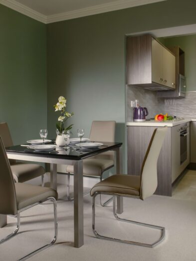 Elegant hotel suite with modern kitchen, dining table, and view of cosy bedroom, offering luxury accommodation.