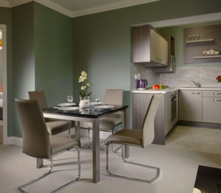 Elegant hotel suite with modern kitchen, dining table, and view of cosy bedroom, offering luxury accommodation.