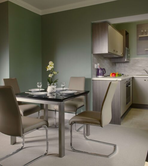 Elegant hotel suite with modern kitchen, dining table, and view of cosy bedroom, offering luxury accommodation.