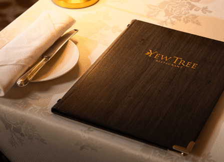 Elegant dining table setup at Yew Tree Restaurant with menu, cloth napkin, and ambient lighting.