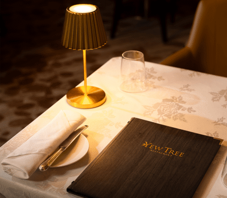 Elegant Yew Tree restaurant table with lamp, menu, white tablecloth, and glassware, offering a cosy dining experience.