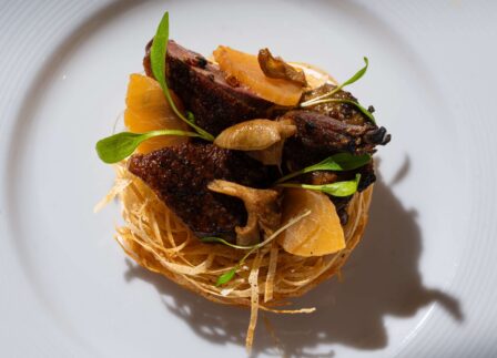 Elegant gourmet dish with roasted figs, crispy basket, and herbs, showcasing fine dining experience at luxury hotel restaurant.