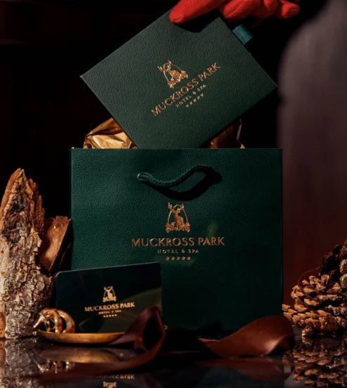Luxurious hotel gift set with elegant bag, candle, and cosy fireplace at Muckross Park Hotel & Spa.
