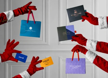 Santa's hands with luxury hotel gift bags against elegant white panelled wall for festive hospitality offerings.