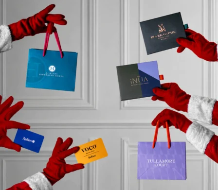Santa's hands with luxury hotel gift bags against elegant white panelled wall for festive hospitality offerings.