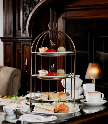 Afternoon tea tiered stand with sandwiches, scones and pastries by a roaring fireplace in Muckross Park Hotel, Monks Lounge