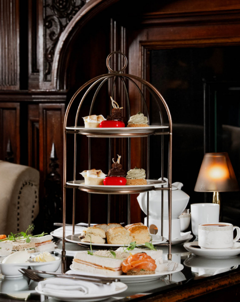 Afternoon tea tiered stand with sandwiches, scones and pastries by a roaring fireplace in Muckross Park Hotel, Monks Lounge