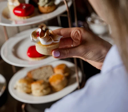 Un huésped toma una tarta de merengue de limón de un soporte de té de tres pisos con bollos, sándwiches y pasteles glaseados: una acogedora experiencia gastronómica en un hotel.