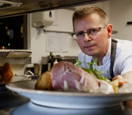 Chef placing a plated meat dish at the kitchen service counter