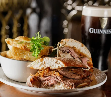 Roast meat sandwiches served with chunky chips beside a pint of Guinness.