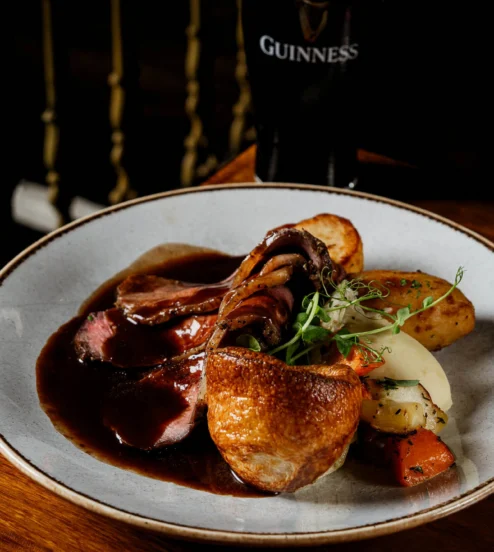 Roast dinner with Yorkshire pudding, sliced beef, pan gravy and roasted veg on a ceramic plate beside a pint, cosy pub dining at Muckross Park Hotel & Spa