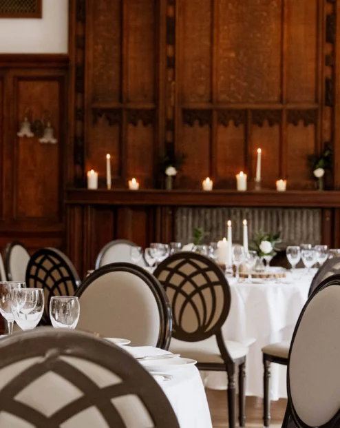 Elegant hotel dining room with round tables, white linens, glassware, decorative lantern centrepieces and candlelit wood panelling atmosphere