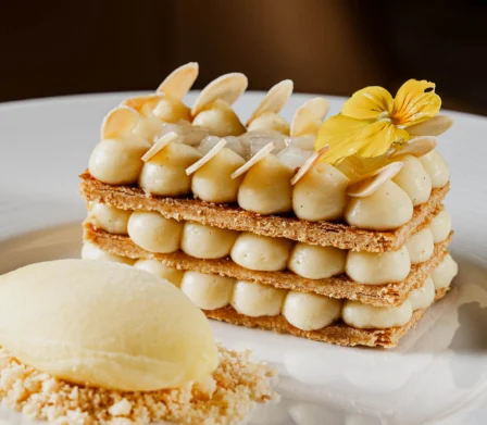 Layered mille‑feuille dessert with piped vanilla cream, almond flakes and edible yellow flower, served with lemon sorbet on crumbbed biscuit — fine dining hotel restaurant