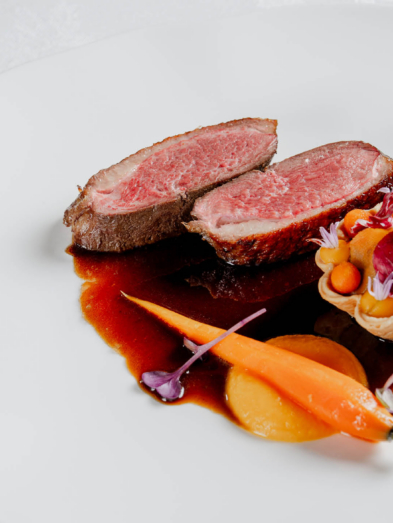 Tranches de rôti à cœur rosé accompagnées d'une tarte glacée aux carottes et aux légumes, le tout présenté sur une assiette blanche.