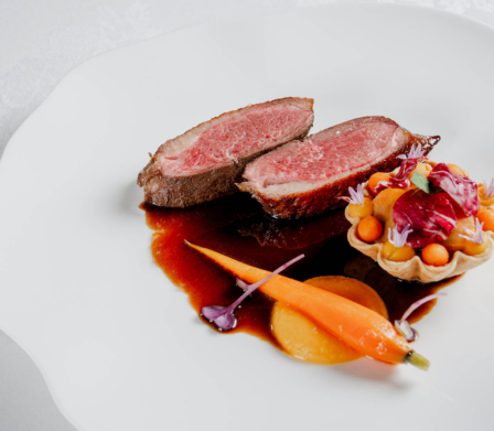 Pan-seared duck breast with rich jus, glazed baby carrot and savoury tartlet on a white linen table for fine-dining hotel restaurant EXPERIENCE